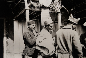 Three soldiers, one smoking a pipe, outside a canteen