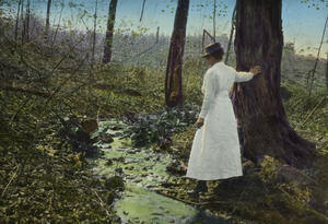Woman standing by a stream in the woods