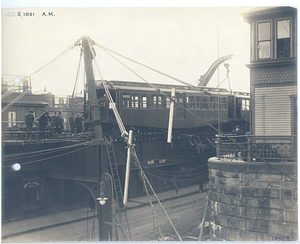 Photograph taken from tracks shows workers making repairs to car recently returned to elevated railway tracks.