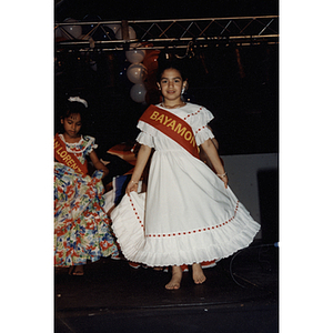Two girls in dresses on stage wearing sashes at the Festival Puertorriqueño