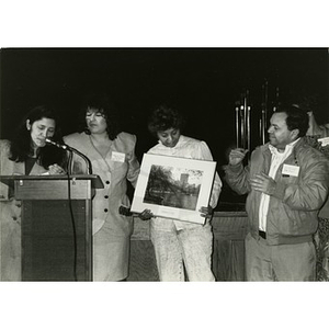 Clara Garcia and Inquilinos Boricuas en Acción board members presenting a framed photograph to a woman on stage.