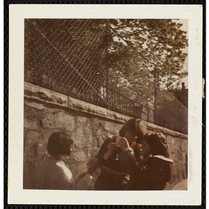 Three girls from the South Boston Boys' Club standing by a fence, two of them looking at something together
