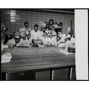 Members of the Tom Pappas Chefs' Club watch a chef work with a pie in a Howard Johnson's kitchen