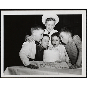 Five boys gather around a cake and blow on its candles