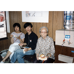 Young man and woman sit eating next to an elderly woman at Asian Community Development Corporation gathering