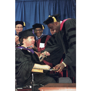 A Law School graduate in a wheelchair receives his diploma from Dean David Hall