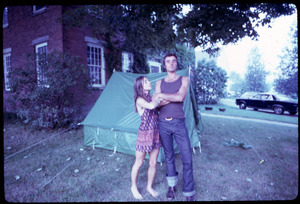 Couple standing in front of a tent pitched on the lawn of a house