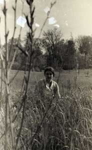 Young woman seated in a field, possibly near the commune house in Warwick