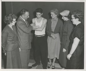 A group of women watch a man with a patient who is a recent below the elbow amputee