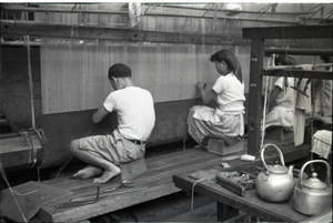 A man and two women working on a large loom