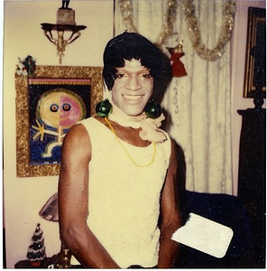 A Photograph of Marsha P. Johnson with a Painted White Face and Green Disco Ball Earrings