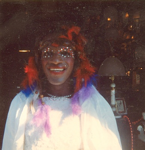 A Photograph of Marsha P. Johnson in a White Dress With Feathers in Her Hair and Gems Around Her Eyes