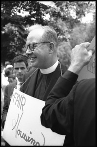 Smiling priest with a 'Fair housing' sign hung around his neck