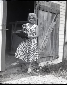Unidentified woman (Vera Guiterman?), standing with cat and portfolio of drawings in the entrance to a barn