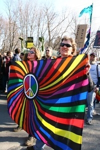 Women holding a banner with rainbow hues and a peace symbol: rally and march against the Iraq War