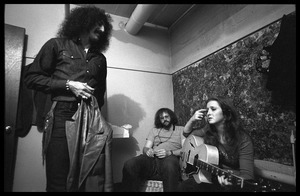 Bonnie Raitt seated backstage with guitar, with Freebo (standing) and John Payne(?)