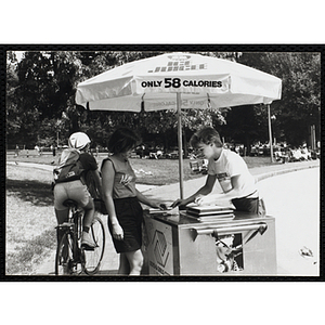 A teenage boy serves ice juice from a food cart to a woman on Boston Common