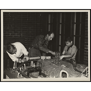 A Man helping two boys set up a model railroad