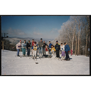 A group of children and adults pose on the top of a mountain at a ski resort