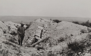 Soldier standing in front of an abandoned dugout entrance, flat fields in the background, Craonne