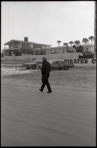 Middle-aged man walking along beach, beach homes in background