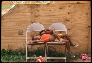 Child with a doll lying on two folder chairs outside a plywood tent at the Resurrection City encampment