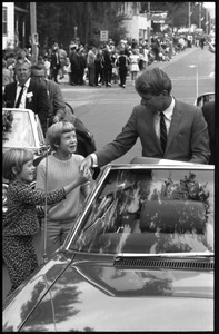Robert F. Kennedy (left) seated in an open car at the Turkey Day parade, shaking hands with a young girl; while stumping for Democratic candidates in the northern Midwest