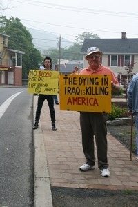 Protesters on the sidewalk holding signs against the War in Iraq reading 'The dying in Iraq is killing America' and 'No blood for oil -- life before profit'