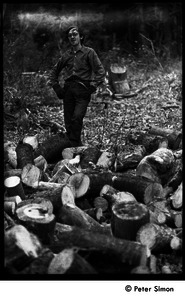 Raymond Mungo posed by a stack of sawn wood, waiting to be split: Packer Corners commune