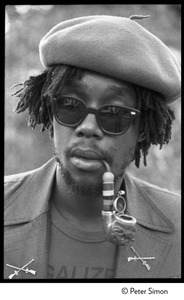 Peter Tosh: portrait wearing beret, dark glasses, and smoking a pipe