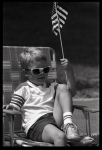 Boy with sunglasses in a lawn chair, waving an American flag and watching the Chesterfield's Fourth of July parade