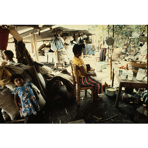 Woman sitting among belongings in an outdoor shelter