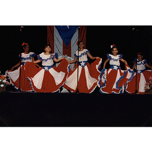 Five girls in Puerto Rican flag dresses dance on stage at the Festival Puertorriqueño