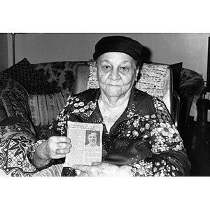 Portrait of an older woman holding up a newspaper clipping about Philip Bradley.