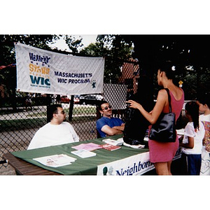 Woman talking with the two men who staff an informational table about the Massachusetts WIC program.