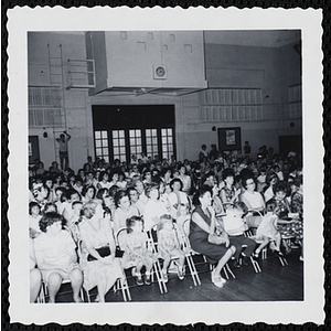 Children and adults, seated in an auditorium, look to the front during a Boys' Club Little Sister Contest