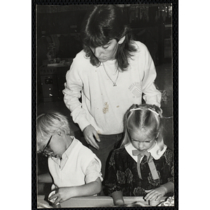 A Teacher observes a young boy and girl working on an arts and crafts project