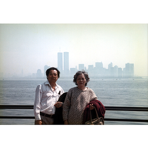 Woman and man stand against a railing across the water from the New York City skyline