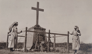 Two Red Cross workers standing next to a large monument of a cross, surrounded by barbed wire, Bayonet Trench, Verdun