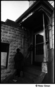 African American woman with broom standing on the front steps of 199 Harvard St., Cambridge, Mass.; banner over doorway reads 'Cambridge is a city, not a highway'