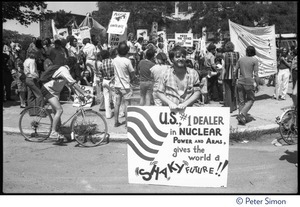 Antinuclear protester with sign reading 'U.S. #1 dealer in nuclear power and arms gives the world a shaky future' and crowd of protesters behind