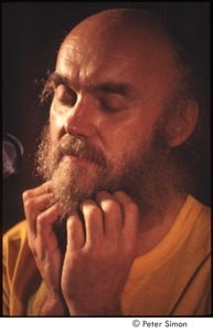 Ram Dass with his hands on his beard, on stage with Amazing Grace