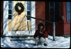 Nina Keller seated in the snow with cat, in front of the door, Montague Farm Commune