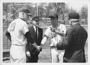 Suffolk University men's baseball player and coach shaking hands as two umpires look on, 1965