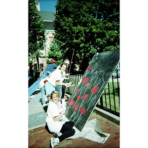 Volunteers painting flowers on a large piece of black plywood.