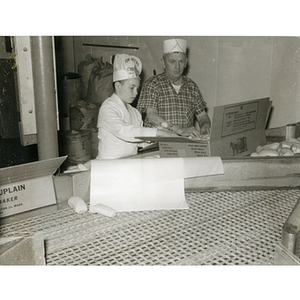 A member of the Tom Pappas Chefs' Club unpacks a box of bread rolls with a kitchen staff member