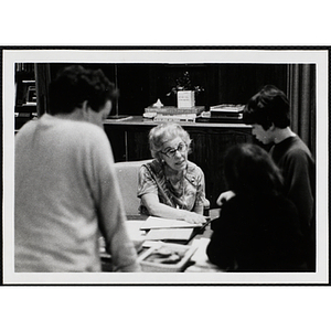 A female staff member sitting at her desk while talking to two boys