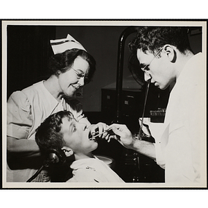 A boy receives a dental exam from a dentist and dental assistant