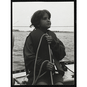 A girl holds a rope on the deck of a sailboat in Boston Harbor