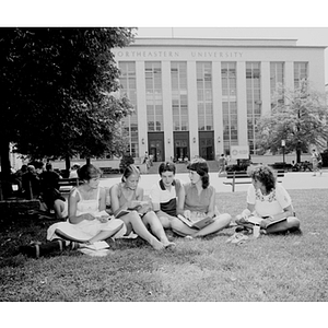 Five students sit in the grass in the quadrangle talking and reading